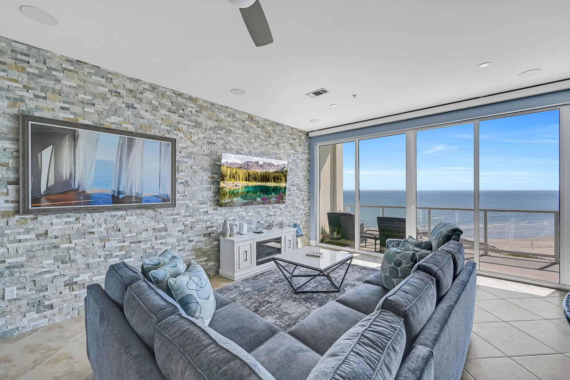 image of a living area open concept with a wide screen TV and large floor to ceiling windows overlooking the beach