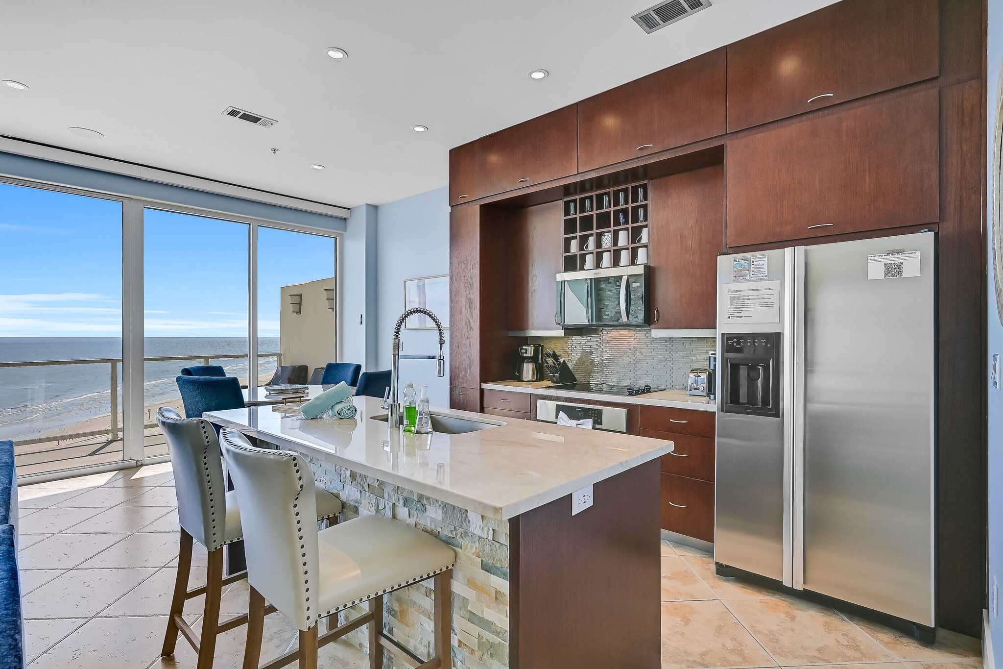 image of a kitchen with and a sink and a stove and a stainless steel refrigerator with a beach view